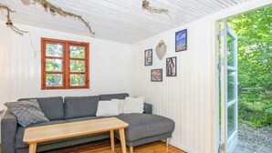 Een knus interieur met een grijze bank, een houten tafel en een groot raam met uitzicht op groen.