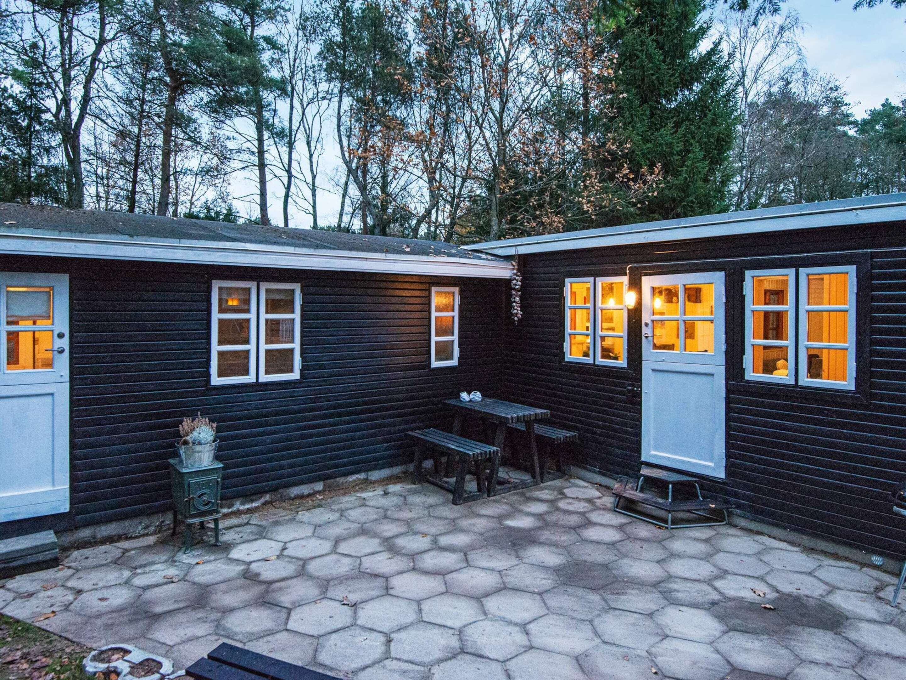 A cabin with two rooms, each with a door and windows, a hexagonal tiled patio, and a small table and bench.