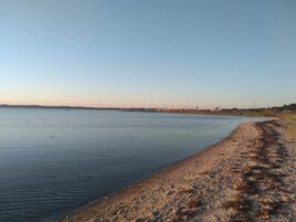 A calm body of water with a sandy shore and distant buildings.