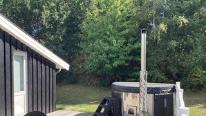A hot tub on a wooden deck with a metal chimney, a table, and chairs. - 6 Person Holiday Home in Ebeltoft (Ebeltoft)