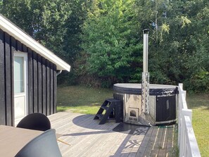 A hot tub on a wooden deck with a metal chimney, a table, and chairs. - 6 Person Holiday Home in Ebeltoft (Ebeltoft)
