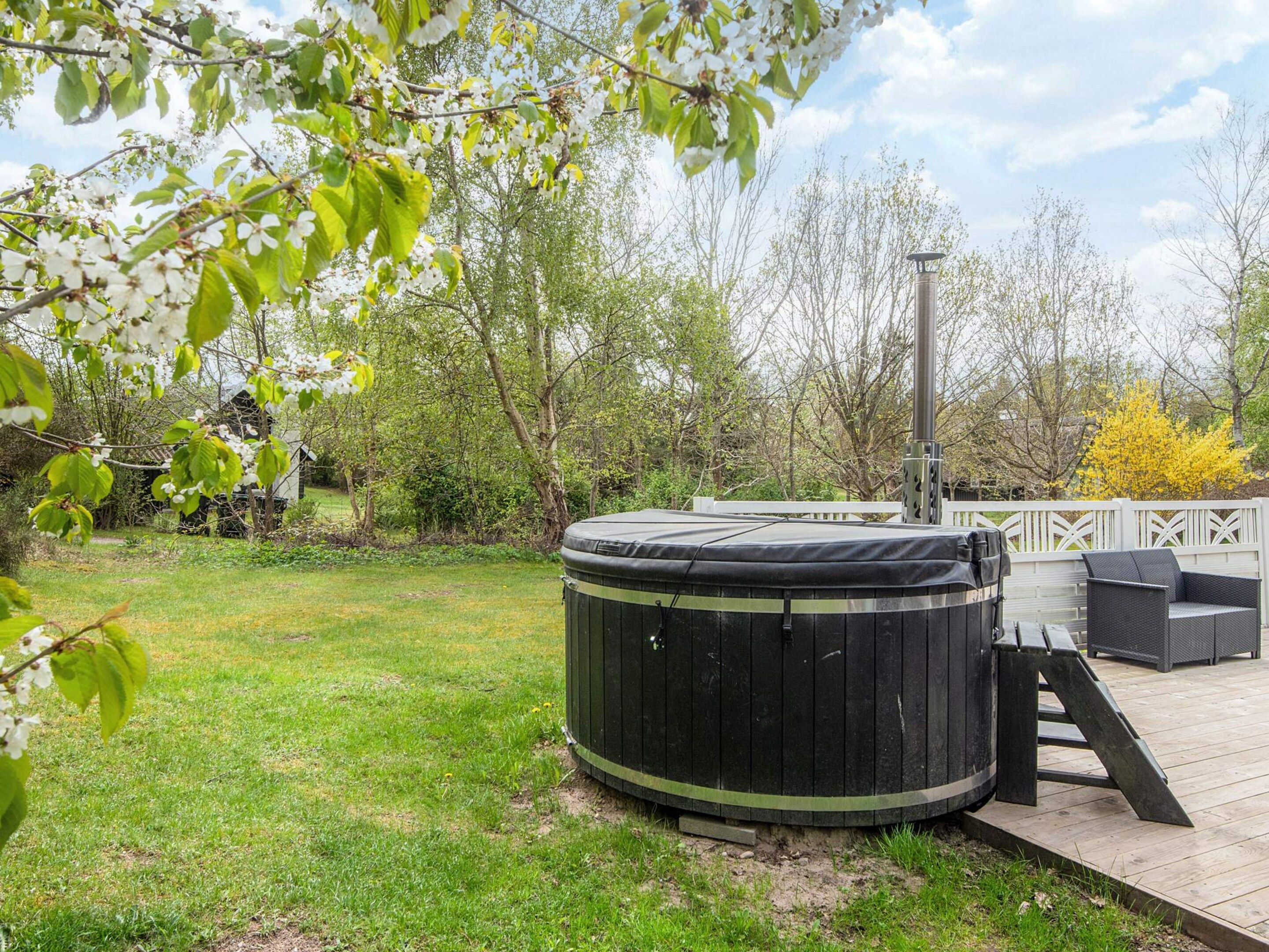 Een hottub op een houten terras, met een witte hek en begroeiing op de achtergrond.