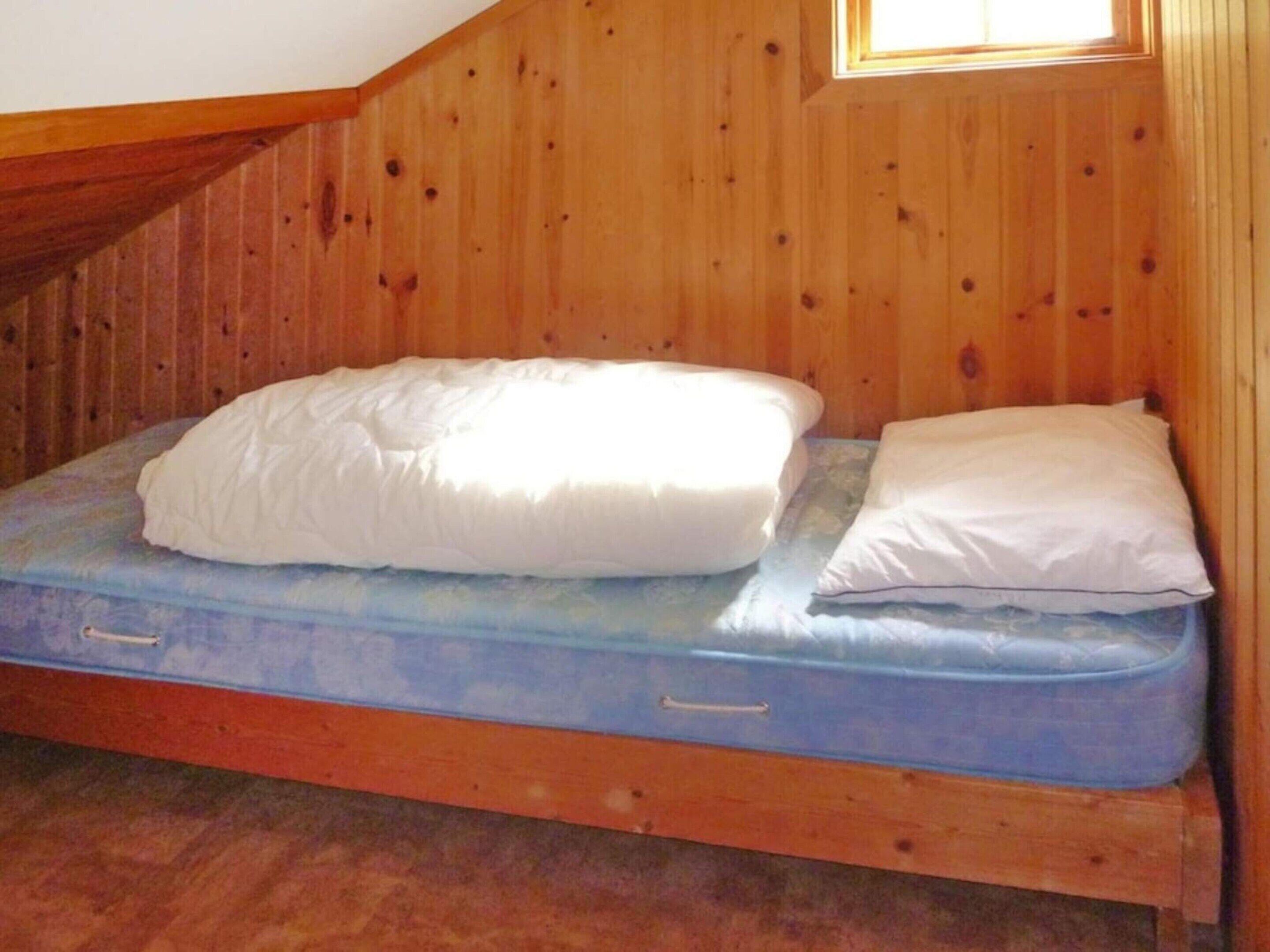 A single bed with a mattress and pillows in a room with wooden walls and a sloped ceiling.