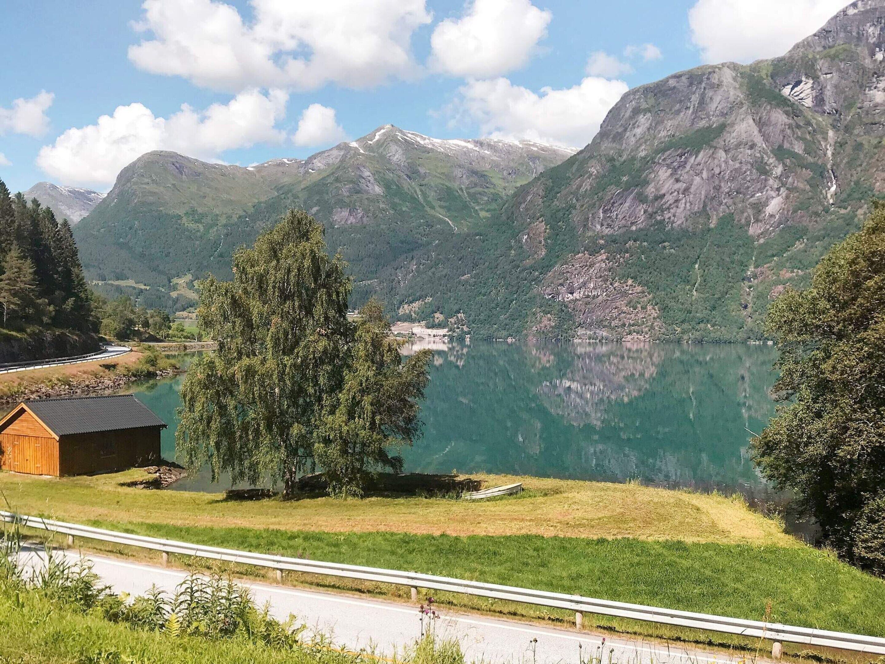 Paesaggio montano con un lago, una baita di legno e una strada.