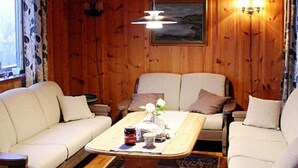 A cozy room with wooden walls, a sofa, a chair, and a table with a painting above. - 7 Person Holiday Home in Oppstryn (Stryn)