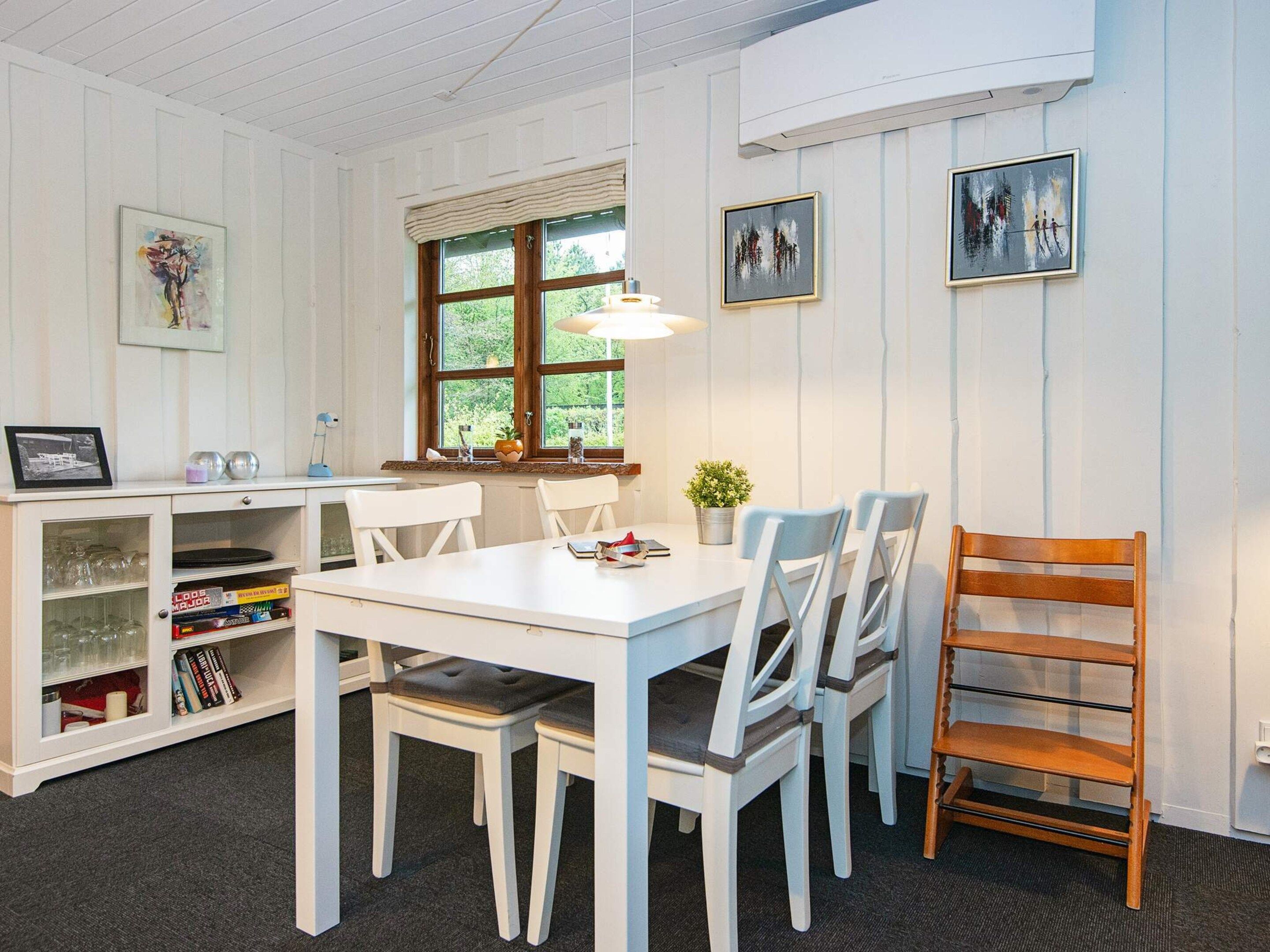 A dining area with a white table, four chairs, a wooden chair, a bookshelf with books, and framed artwork on the wall.