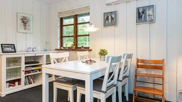 A dining area with a white table, four chairs, a wooden chair, a bookshelf with books, and framed artwork on the wall.