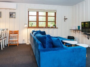 A room with a blue sofa, a small table, a TV, and a window with a view of greenery. - 4 Person Holiday Home in Toftlund (Toftlund)