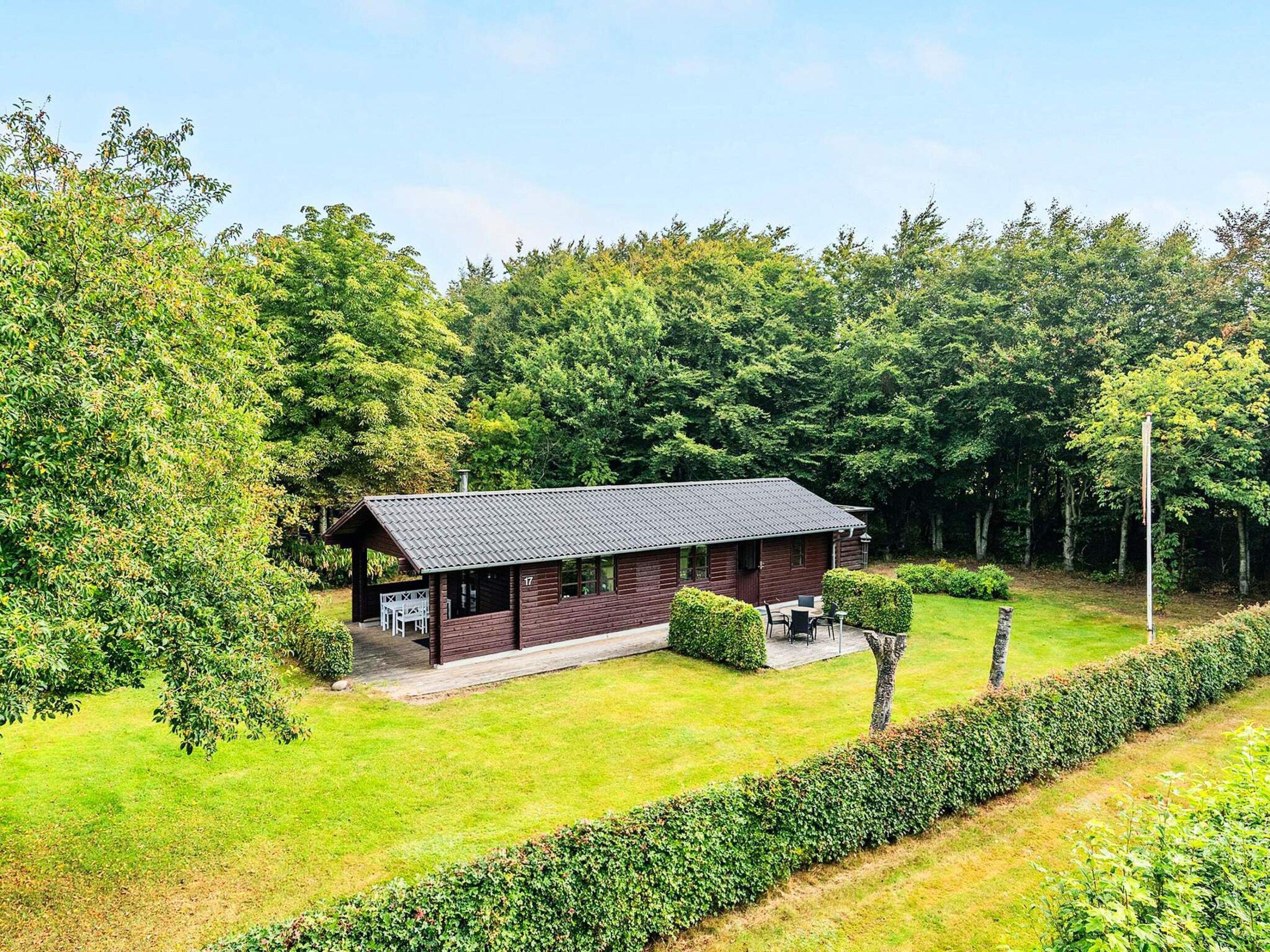 A cabin with a sloped roof, surrounded by a well-maintained lawn and dense forest.