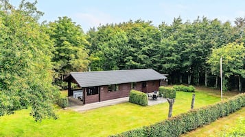 A cabin with a sloped roof, surrounded by a well-maintained lawn and dense forest.