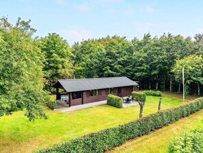 A cabin with a sloped roof, surrounded by a well-maintained lawn and dense forest. - 4 Person Holiday Home in Toftlund (Toftlund)