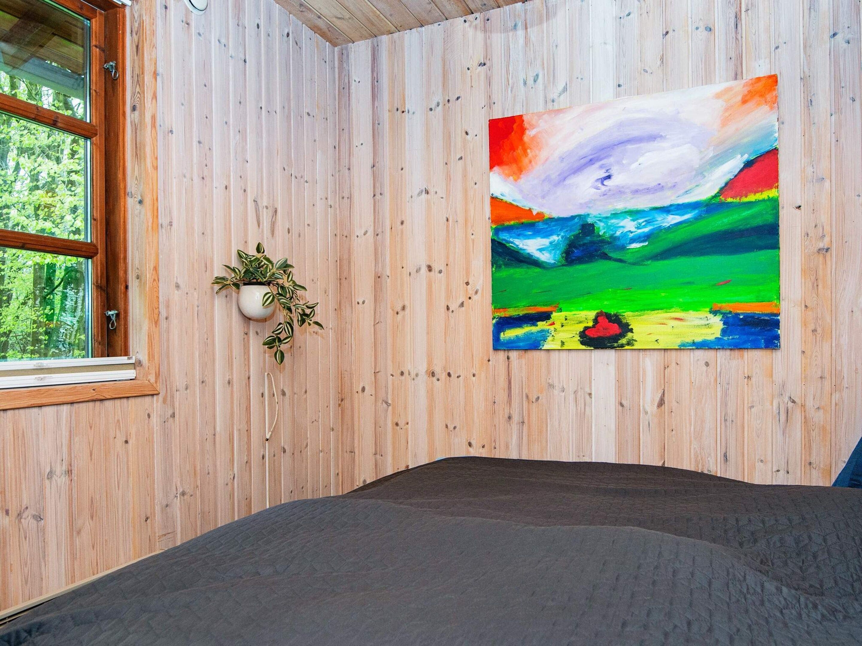 A room with a bed, a window, a wall-mounted plant, and a colorful abstract painting.