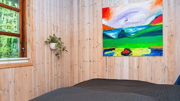 A room with a bed, a window, a wall-mounted plant, and a colorful abstract painting.