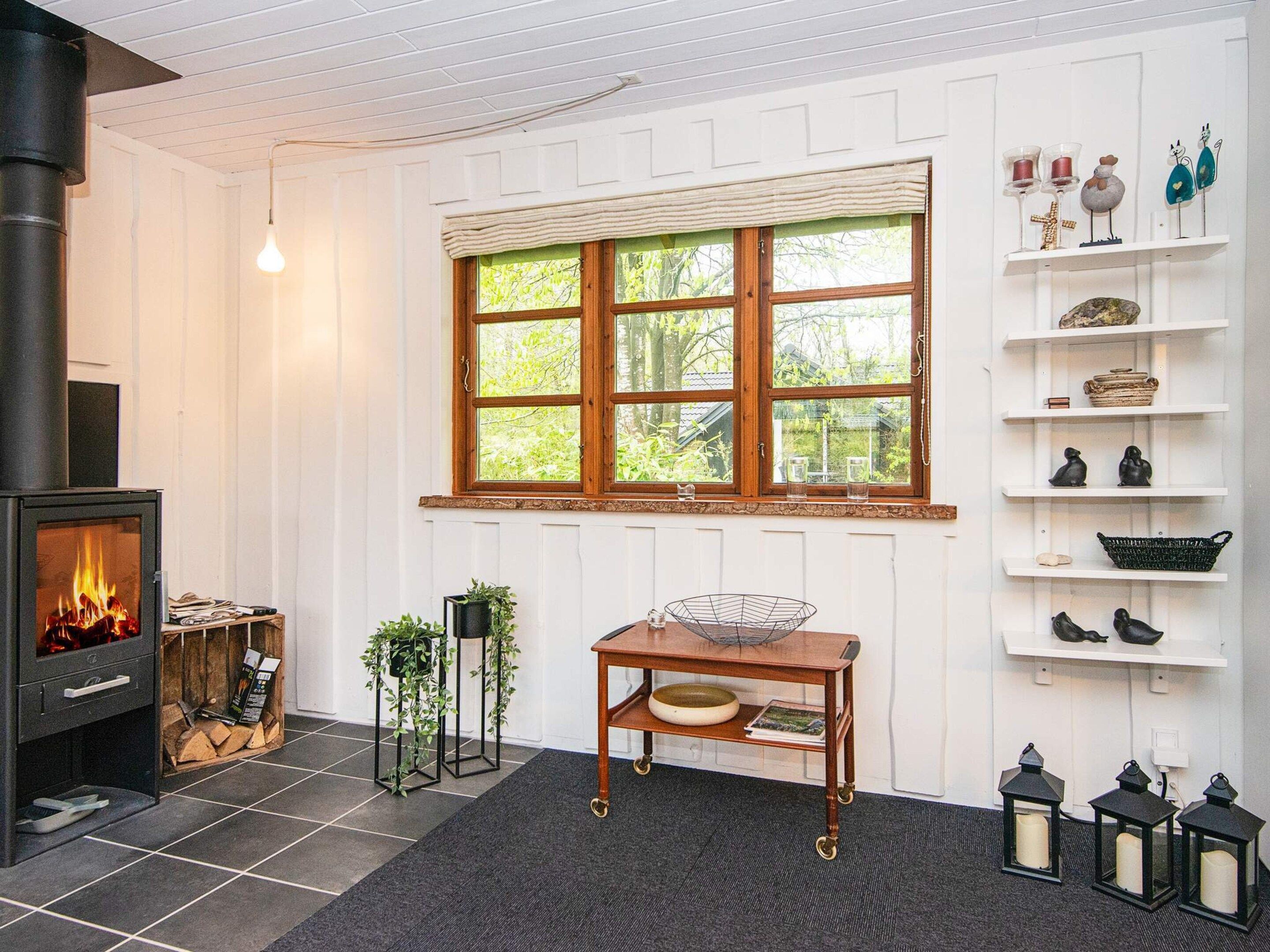 Um quarto aconchegante com lareira, janela com vista, prateleira com objetos decorativos e mesa com uma tigela.