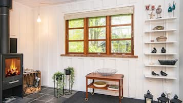 A cozy room with a fireplace, a window with a view, a shelf with decorative items, and a table with a bowl.