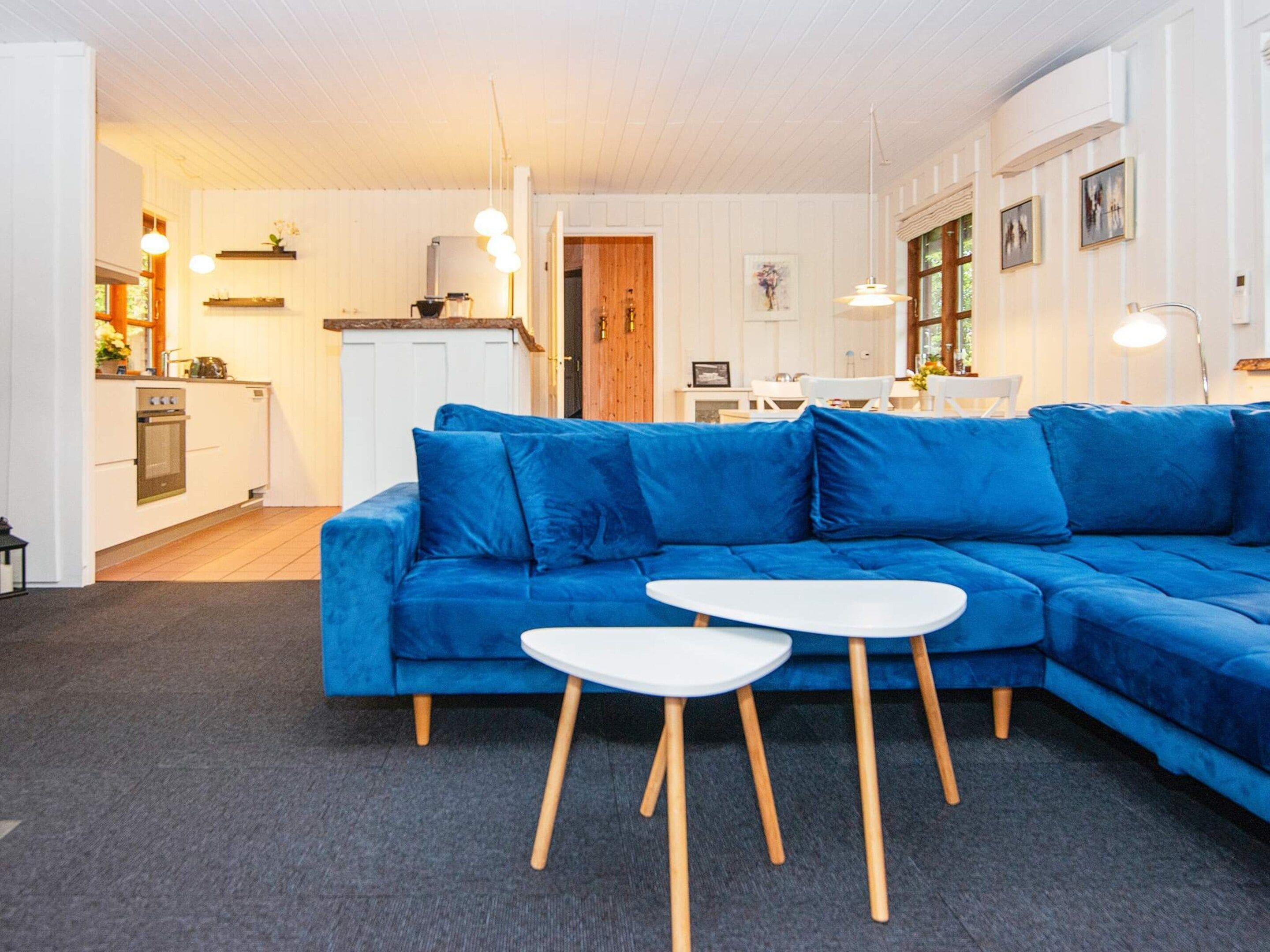 A modern living room with a blue sectional sofa, a white coffee table, and a kitchen area in the background.