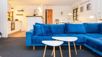 A modern living room with a blue sectional sofa, a white coffee table, and a kitchen area in the background.