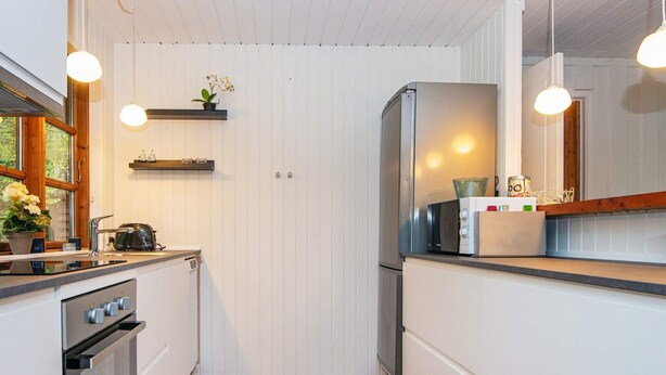 A kitchen with white cabinetry, a stainless steel refrigerator, a microwave, and a toaster on the counter. There are hanging pendant lights, a window with a view, and a door with a small plant on the wall.