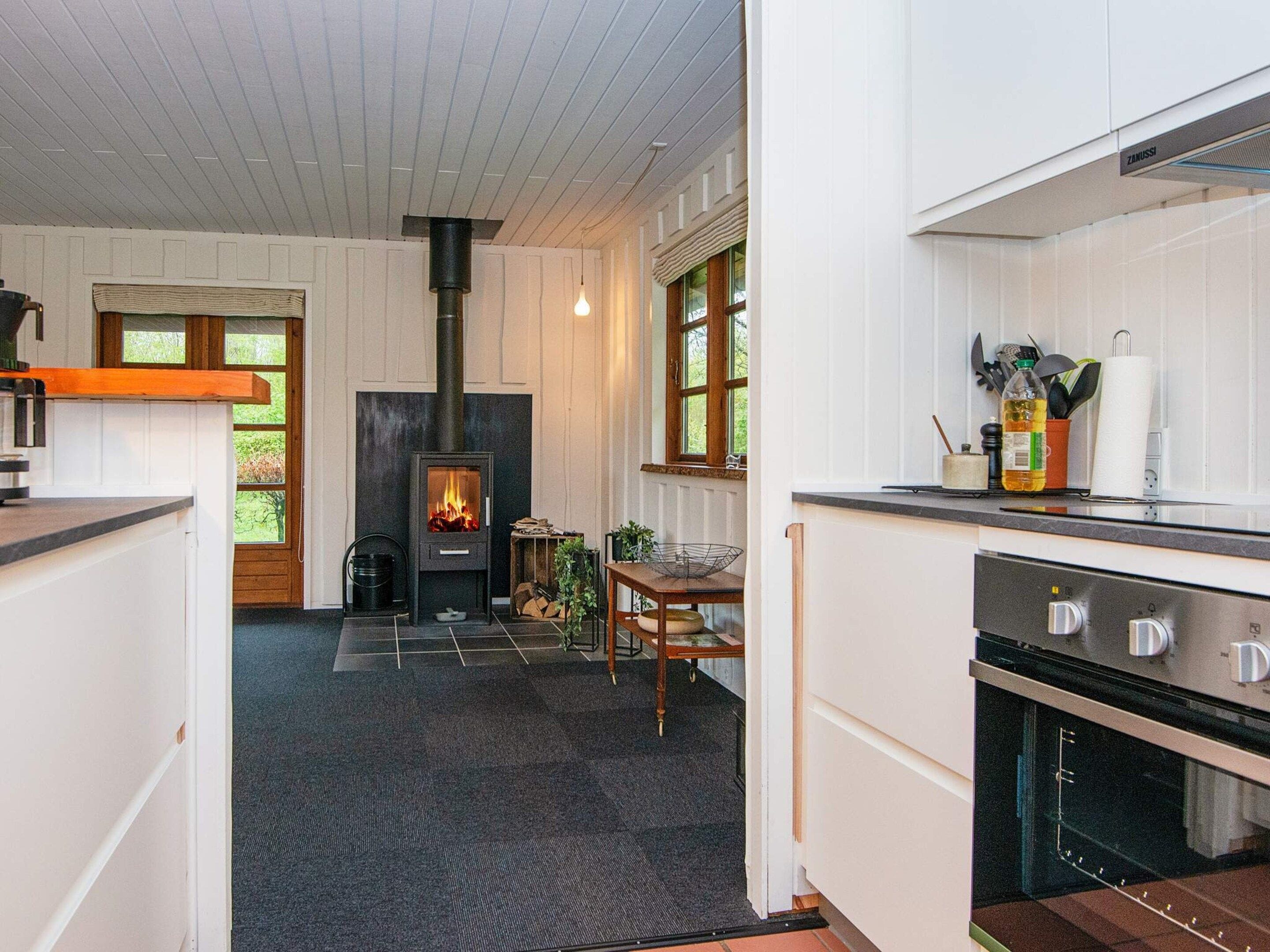 A modern kitchen with a built-in wood stove, a dining area with a table and chairs, and a view of the outdoors through large windows.