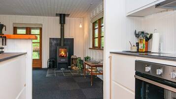 A modern kitchen with a built-in wood stove, a dining area with a table and chairs, and a view of the outdoors through large windows.