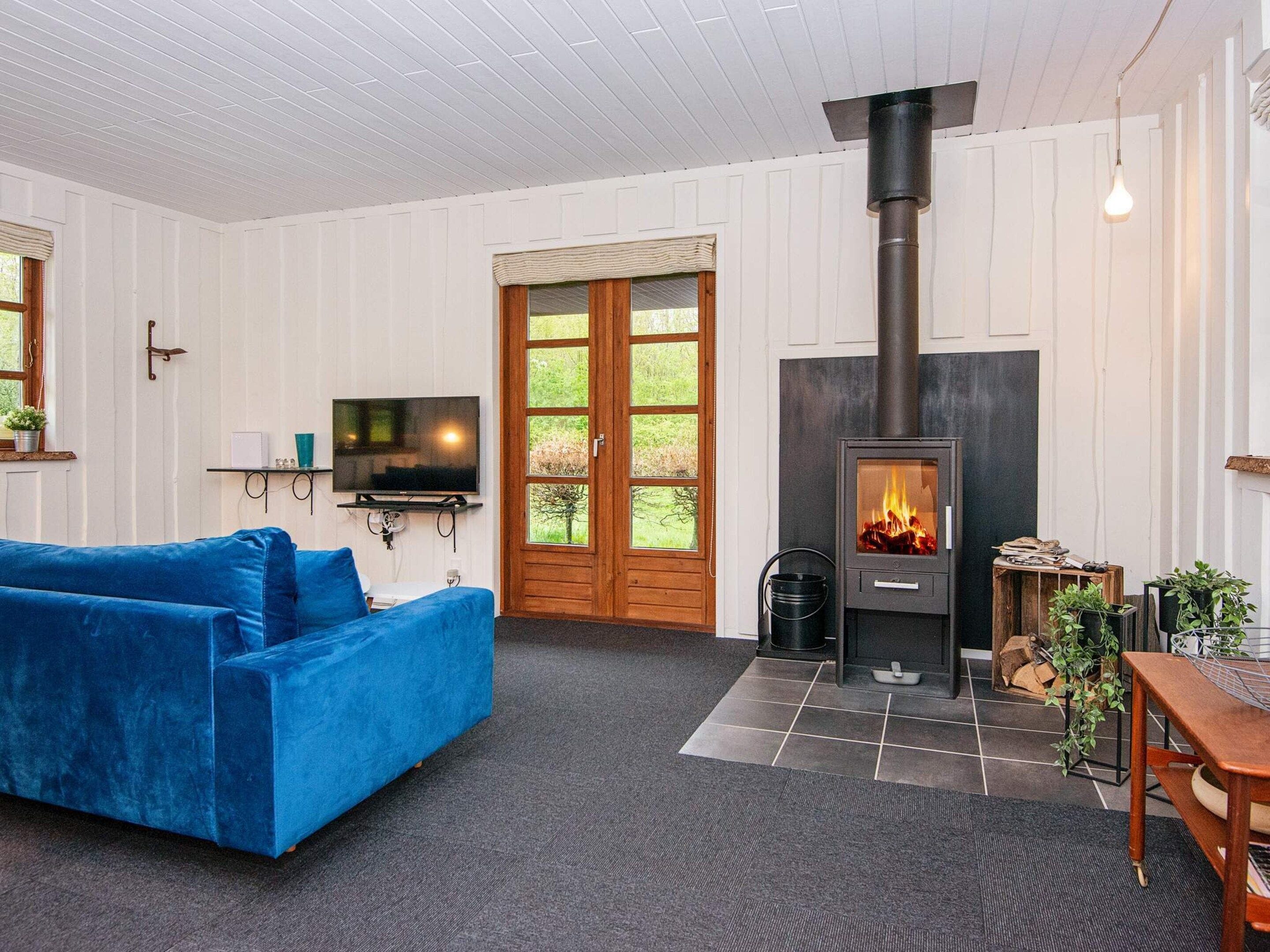 A cozy living room with a blue sofa, a television, a fireplace, and a large window.
