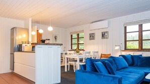 A modern kitchen with white cabinets, a built-in fridge, and a dining area with a blue sofa and white chairs.