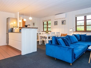 A modern kitchen with white cabinets, a built-in fridge, and a dining area with a blue sofa and white chairs. - 4 Person Holiday Home in Toftlund (Toftlund)