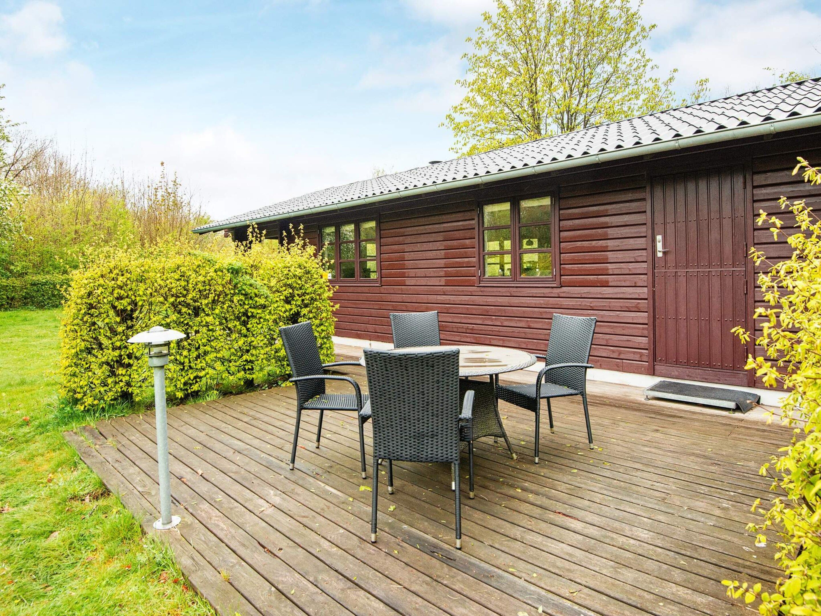 Une terrasse en bois avec une table et des chaises, un lampadaire et un bâtiment à l’extérieur d’un rouge foncé, doté de fenêtres.