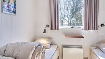 A bedroom with two beds, a window with curtains, a radiator, and a wall-mounted lamp.