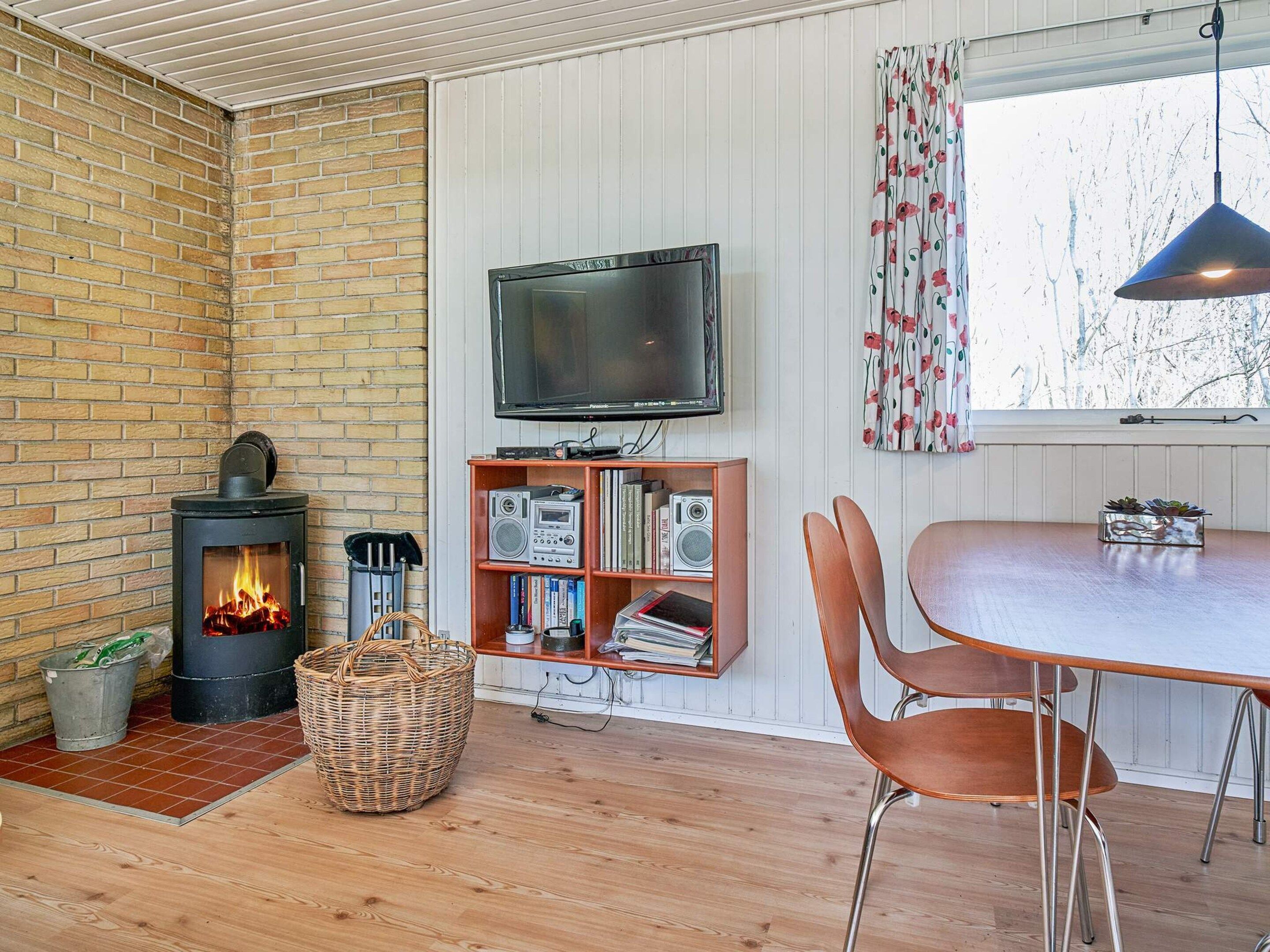 A cozy room with a brick wall, a fireplace, a television, a bookshelf, and a dining area.