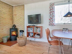 A cozy room with a brick wall, a fireplace, a television, a bookshelf, and a dining area. - 4 Person Holiday Home in Aakirkeby (Akirkeby)