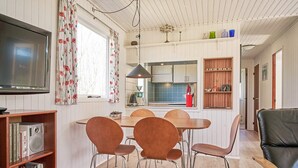 A modern living room with a TV, a dining area with chairs, a bookshelf, and a kitchen in the background. - 4 Person Holiday Home in Aakirkeby (Akirkeby)