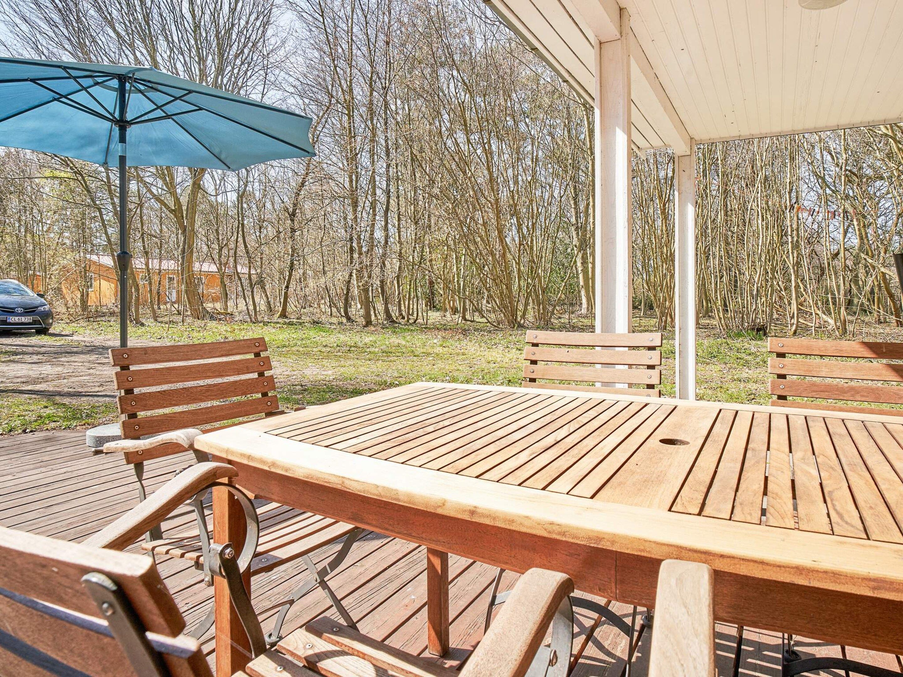 A wooden deck with a table and benches, surrounded by trees.