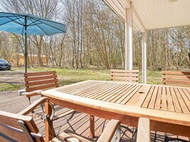 Una terraza de madera con una mesa y bancos, rodeada de árboles.
