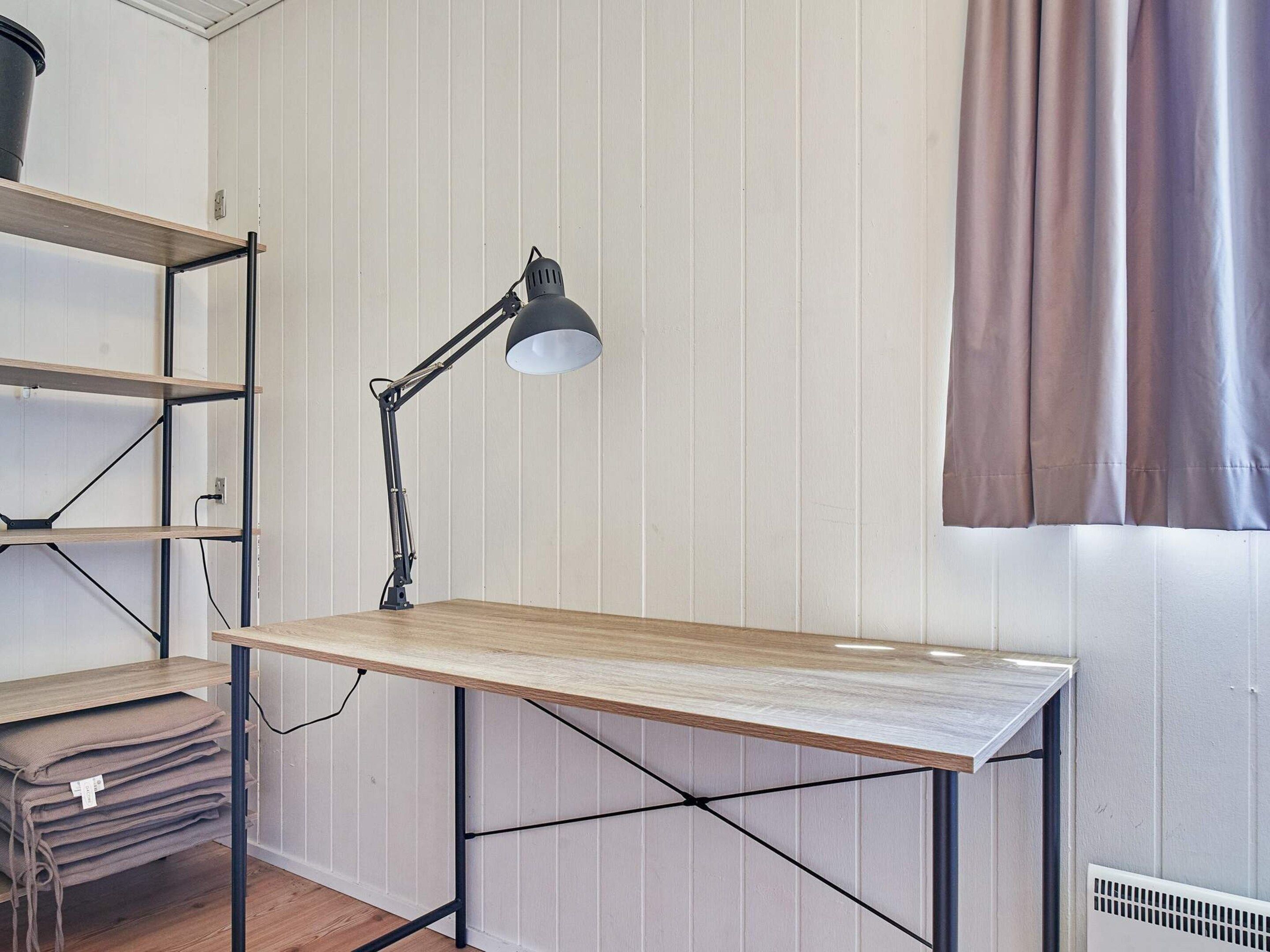 A workspace with a wooden desk, a black desk lamp, and metal shelving units against a paneled wall.