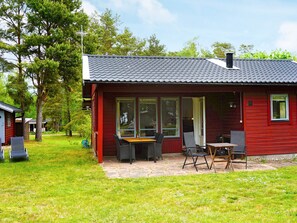 A red wooden cabin with a tiled roof, a patio with a table and chairs, and a grassy yard. - 6 Person Holiday Home in Monsteras (Monsteras)