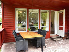 A covered patio with a wooden table and four chairs, large windows, and a stone floor. - 6 Person Holiday Home in Monsteras (Monsteras)