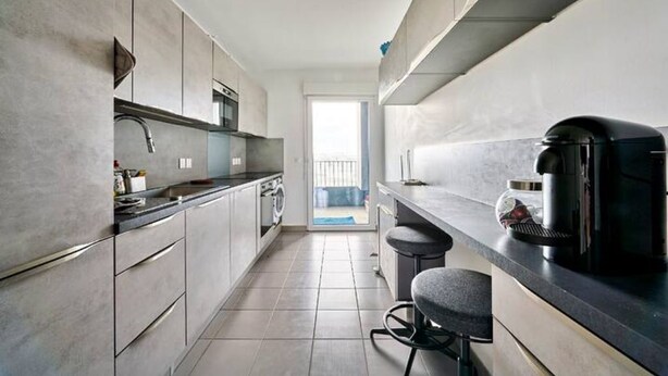 Une cuisine moderne avec des meubles gris, un four encastré et une machine à café.