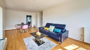 Un salon moderne avec un canapé bleu foncé, une table basse et un coin repas avec des chaises roses.
