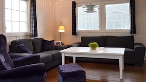 A living room with a dark grey sofa, a white coffee table, and a purple ottoman. There are two windows with black curtains, a hanging lamp, and a small plant on the coffee table. - 4 Person Holiday Home in Utvik-by Traum (Stryn)