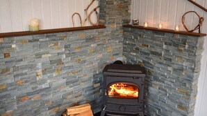A stone fireplace with a wood-burning stove, a copper wood storage container, and a black rug on the floor. - 4 Person Holiday Home in Utvik-by Traum (Stryn)