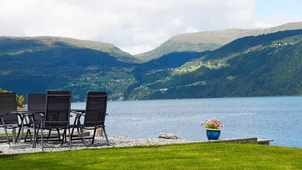 A lakeside seating area with chairs and a flower pot, overlooking a lake with hills in the background. - 4 Person Holiday Home in Utvik-by Traum (Stryn)