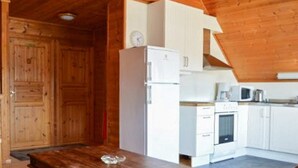 A wooden interior with a wooden table, white cabinets, a refrigerator, a microwave, and a stove. - 4 Person Holiday Home in Maloy-by Traum (Kinn)