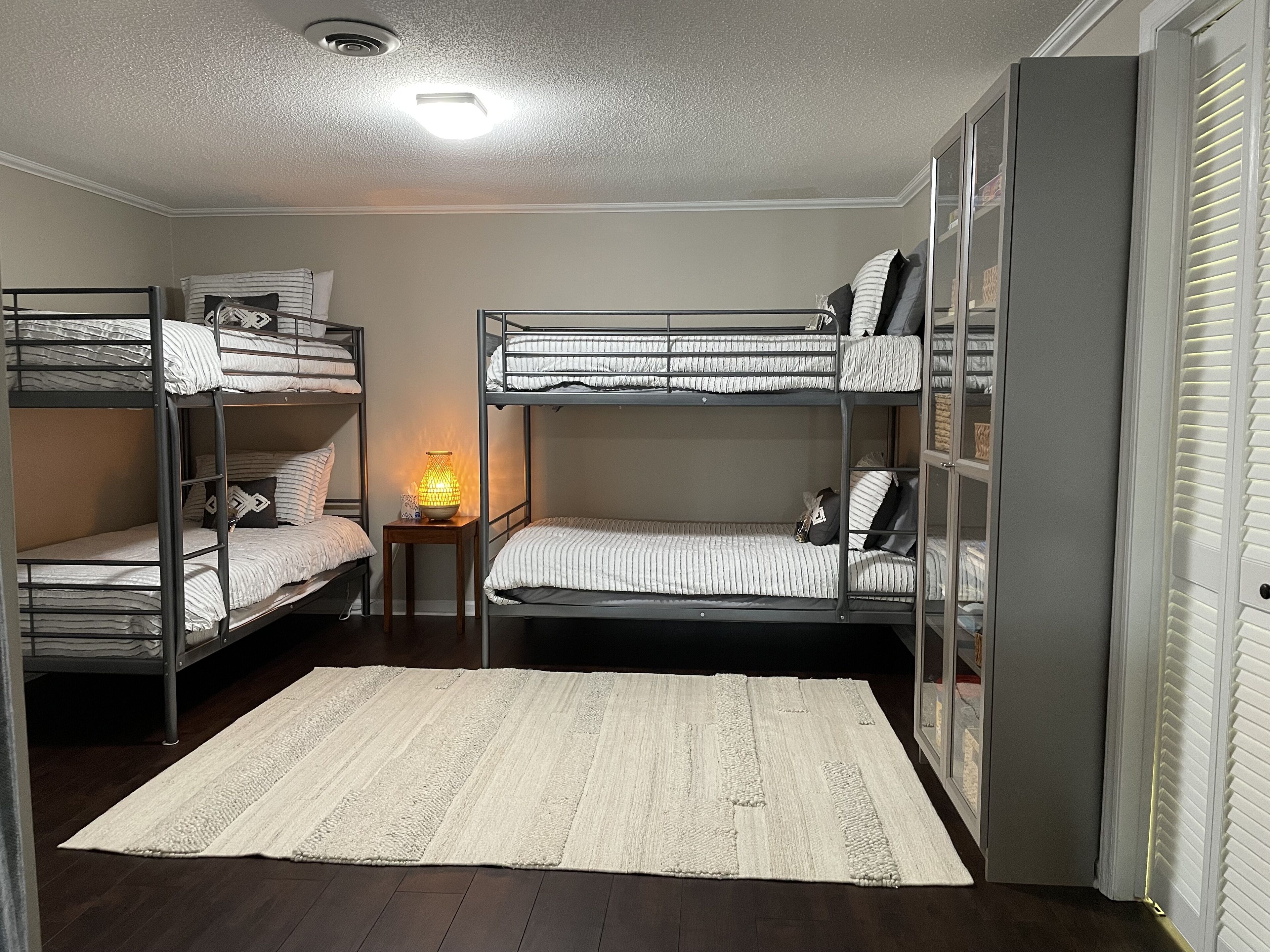 Ein Schlafsaalzimmer mit Etagenbetten, einem kleinen Tisch mit Lampe und einem weißen Teppich.