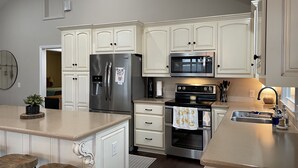 A modern kitchen with white cabinetry, stainless steel appliances, and a central island with stools. - Lake Front House with Dock, Kayaks, and Boat Slip (Troy)