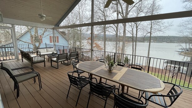 A covered outdoor deck with a table and chairs, overlooking a lake with boats. - Lake Front House with Dock, Kayaks, and Boat Slip (Troy)