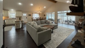 A spacious living area with a large gray sectional sofa, a dining table with chairs, and a kitchen with white cabinets. - Lake Front House with Dock, Kayaks, and Boat Slip (Troy)