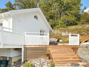 Un bâtiment blanc avec un toit en pente, une terrasse en bois et un mur en pierre.