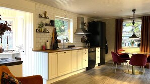 Eine moderne Küche mit weißen Schränken, einem schwarzen Kühlschrank und einem Essbereich mit einem runden Tisch und roten Stühlen.