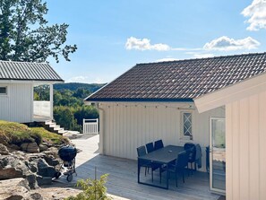 Un espace extérieur abrité, doté d’une table et de chaises, d’un barbecue et offrant une vue sur un paysage boisé.